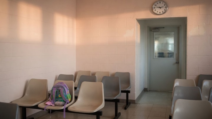 Empty chairs in a quiet facility waiting room with a child’s backpack — families waiting on visitation day