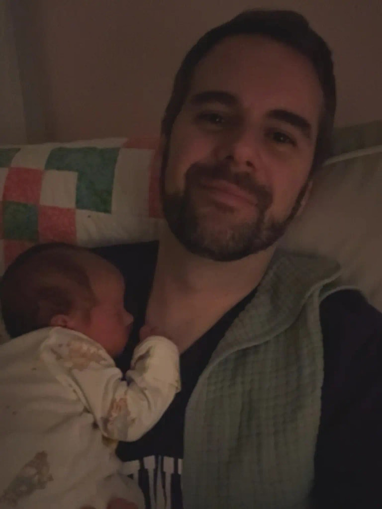 A man holding a sleeping newborn girl against his chest at home